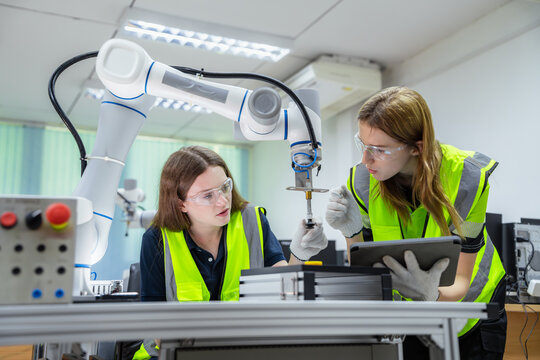 Two women in yellow vests are working on a robot. Concept of Industry 4.0 with diverse engineers collaborating on automation technology.