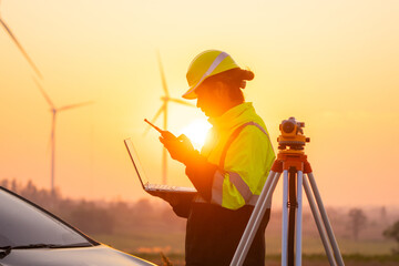 Engineer working on laptop in front of wind turbines for checking wind turbines of the field during beautiful sunset. Alternative energy concept.