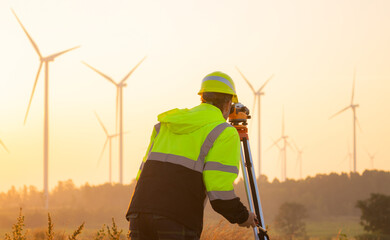 Engineer working in front of wind turbines for checking wind turbines of the field during beautiful sunset. Alternative energy concept.