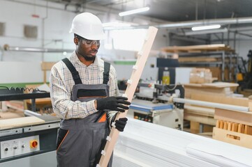 Carpenter holding wooden plank in furniture factory