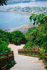 Vertical orientation of wooden walkway trail with handrail going up Seongsan Ilchulbong volcano, also called Sunrise Peak, with city and beach below in Seogwipo, Jeju Island, South Korea