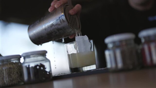 Static close-up clip shows bartender pouring vibrant citrus cocktail from shaker into glass with ice. Focus on liquid flow and condensation. Perfect for cocktail or bartender reels.