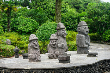 Several stone grandfather statues on Jeju Island in South Korea with forest in background
