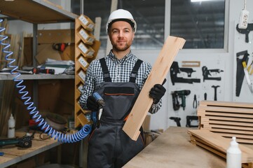 Carpenter holding wooden plank and nail gun in furniture factory