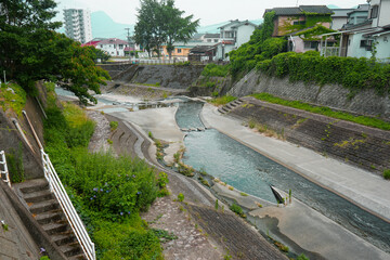 Water drainage river with staircase and foliage going through a residential area of town along a walking path near Beppu University in Beppu, Oita, Japan