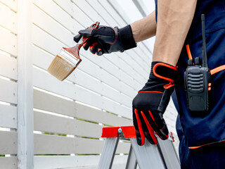 Male painter or decorator hand in protective gloves holding paintbrush while standing on the ladder...