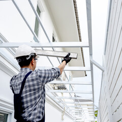 Roof installation process. House extension and renovation. Male roofer in protective workwear installing steel beam at building site. Construction worker man lifting metal part of roof structure.
