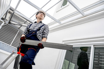 Roof installation process. Asian man roofer in protective workwear standing on the ladder...