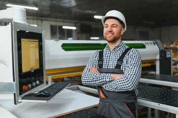 Furniture maker smiling with arms crossed by cnc machine in factory
