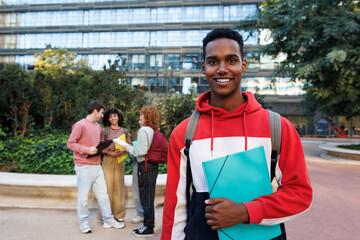 Smiling college student holding a binder on campus with friends in background