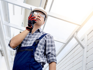 Confident Asian man civil engineer looking forward and talking on walkie talkie. Smart male foreman using radio communication equipment at construction site for cooperation with the worker team