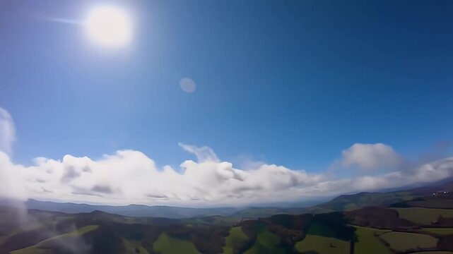 Aerial shot of rolling green hills under cloudy blue sky, mist veiling the landscape