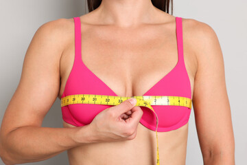 Woman in beautiful bra measuring breast circumference on light grey background, closeup