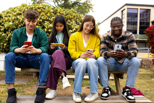 University students using smartphones on bench in campus park - Powered by Adobe