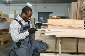African american Carpenter checking wooden plank in furniture factory
