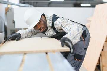 African american Carpenter working with wood panel on cnc machine in furniture factory