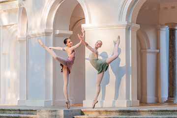Two young ballerinas perform arabesque on stone steps in a park.