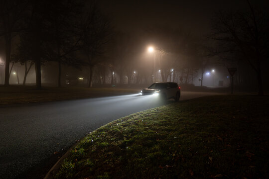 Headlights from a white SUV illuminate mist on a foggy night