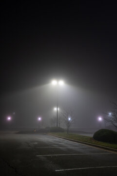 Street lights illuminate mist on a foggy night in a parking lot