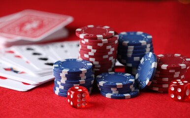 Casino chips, playing cards and dice on red table, closeup