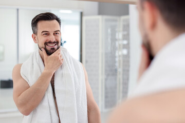 Smiling man before shaving looking at mirror in bathroom