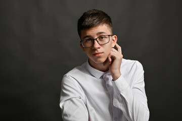 boy with glasses looks ahead, scratches behind his ear, ponders what to answer. gesture of...
