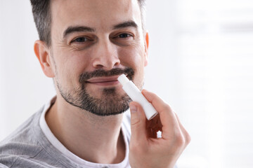 Handsome man applying lip balm onto his lips on blurred light background
