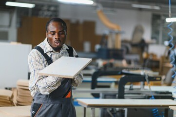 Carpenter blowing dust off wooden plank in furniture factory