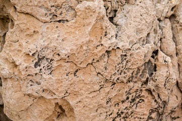 Close-up of a rough rock surface with visible cracks and natural erosion lines.beige stone showing surface irregularities, weathering marks, and natural patterns. textured stone background with cracks