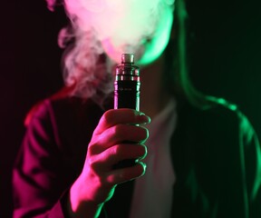 Woman using electronic smoking device in neon lights on black background, closeup