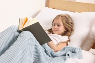 Little girl reading book in bed at home