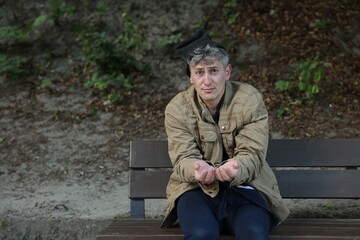 Homeless man begging for money on bench in park, space for text