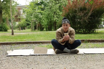 Poor man with sign Homeless and paper cup begging for money on carton in park