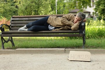 Poor man sleeping on bench and sign Homeless in park