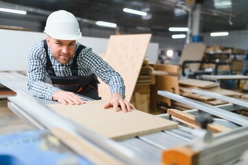 Carpenter working with wood panel on cnc machine in furniture factory