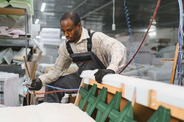 Furniture maker applying glue on sofa with spray gun in factory