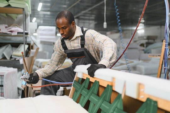 Furniture maker applying glue on sofa with spray gun in factory
