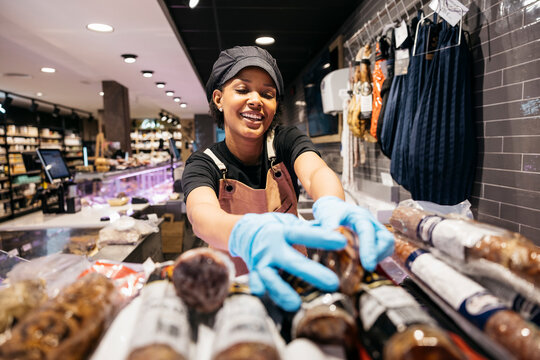 Smiling butcher arranging sausages inside refrigerated display of gourmet supermarket