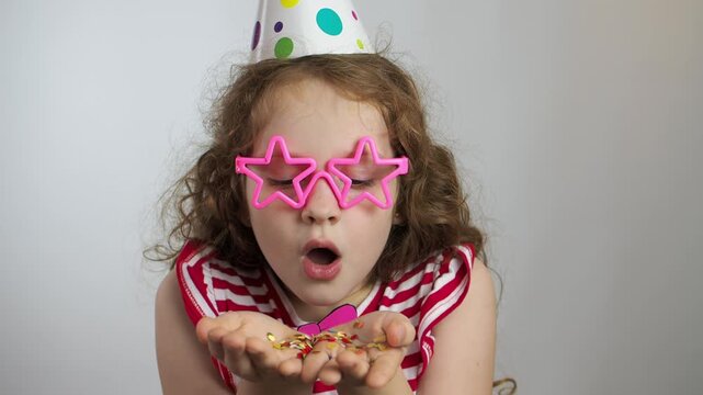 Little girl blowing rainbow confetti. Holiday birthday concept.