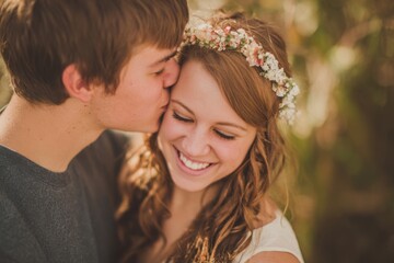 Naklejka premium Happy young couple sharing a kiss outdoors on a sunny day with joyful expressions.