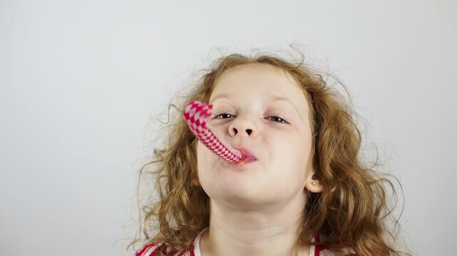 Happy little girl blows a festive pipe on a light background. Holiday birthday concept.