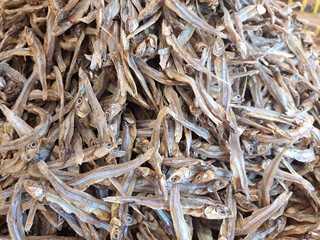 A detailed shot of numerous dried anchovies stacked together, showcasing texture and natural detail, captured in a market setting. Perfect for food, culinary, or traditional market-related purposes.