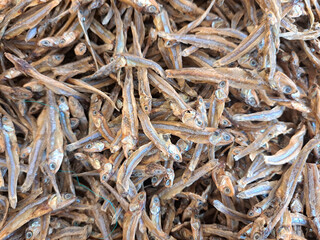 A detailed shot of numerous dried anchovies stacked together, showcasing texture and natural detail, captured in a market setting. Perfect for food, culinary, or traditional market-related purposes.
