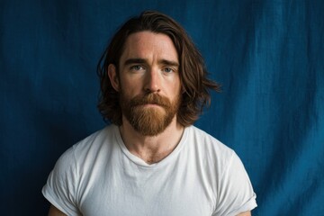 Obraz premium Portrait of a Bearded Man with Long Wavy Hair and Casual White T-Shirt Against Blue Background.