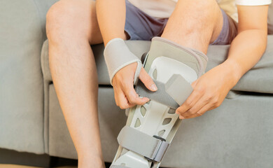 Man take-off ankle orthosis on leg sitting on the sofa at home. Ankle foot orthosis.