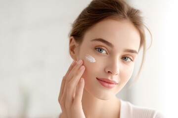Obraz premium Young woman applying skincare cream to face with natural light in bright room.