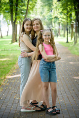beautiful blonde smiling mother and two daughters with long hair posing in summer park. Happy hugging family