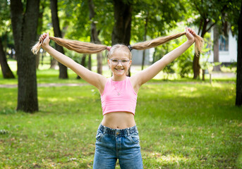 funny happy smiling little girl in glasses in pink top and jeans  posing in park on sunny summer day