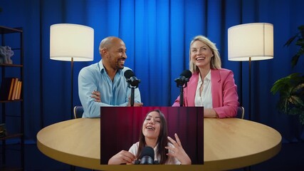 Two hosts engage in a lively podcast discussion with a remote guest appearing on a screen. The hosts listen, interact, and react with interest and amusement