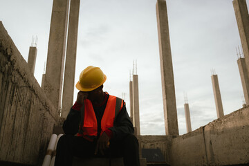 Frustrated male construction engineer wearing a hard hat looks stressed and overwhelmed at a job...
